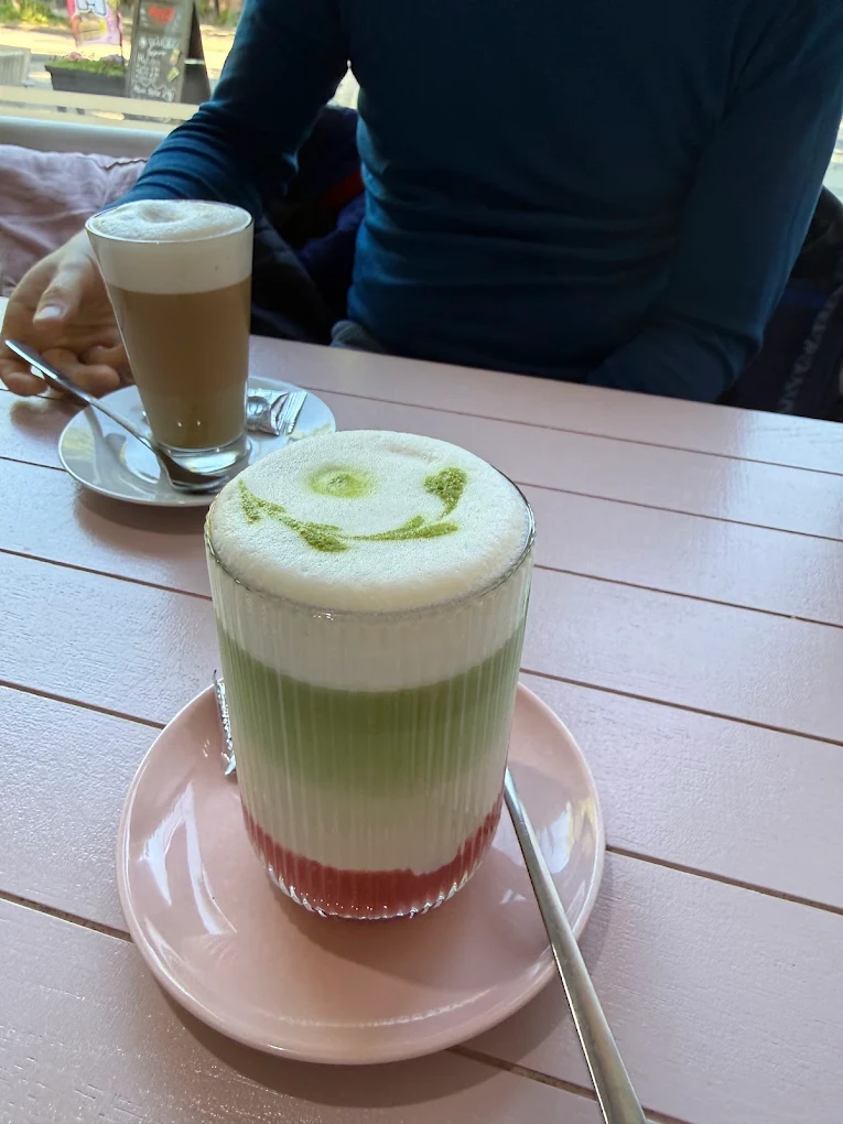 Matcha-Latte mit Schaumherz und Latte Macchiato auf rosa Tisch im Café Paradiso