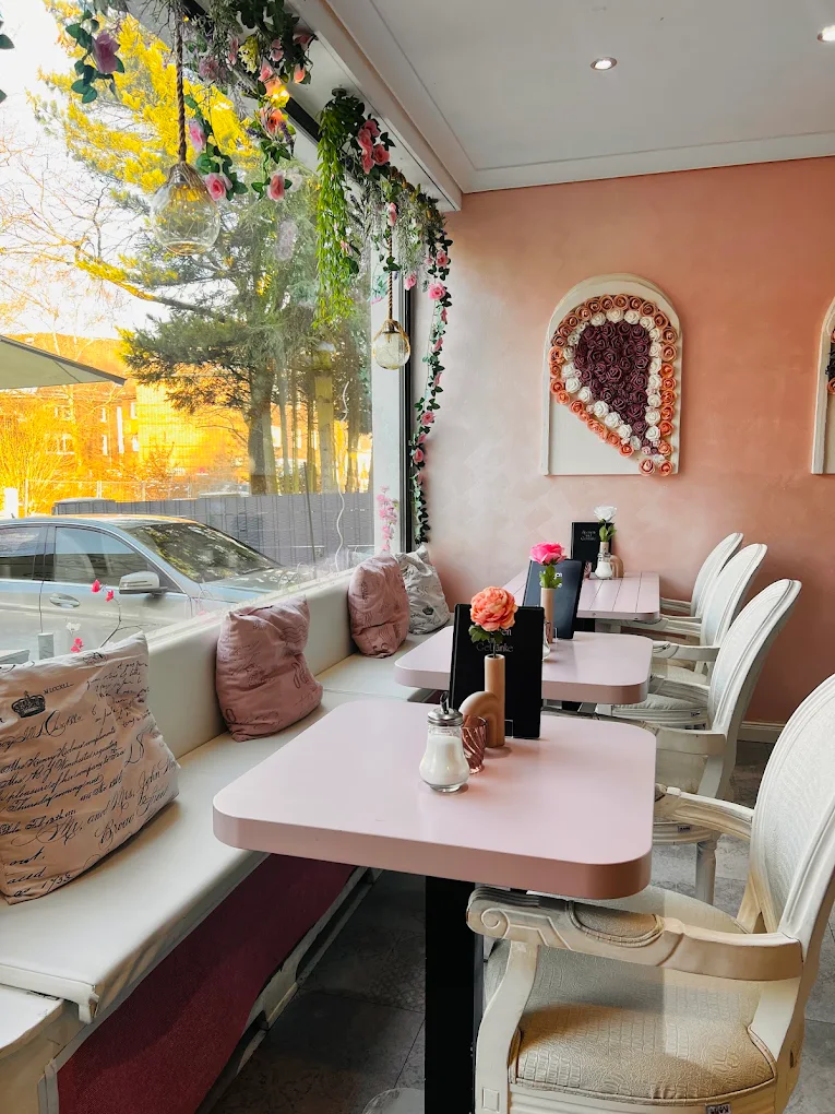 Fensterplatz im Café Paradiso mit rosa Tischen, Blumenranken und Rosenherz an der pfirsichfarbenen Wand